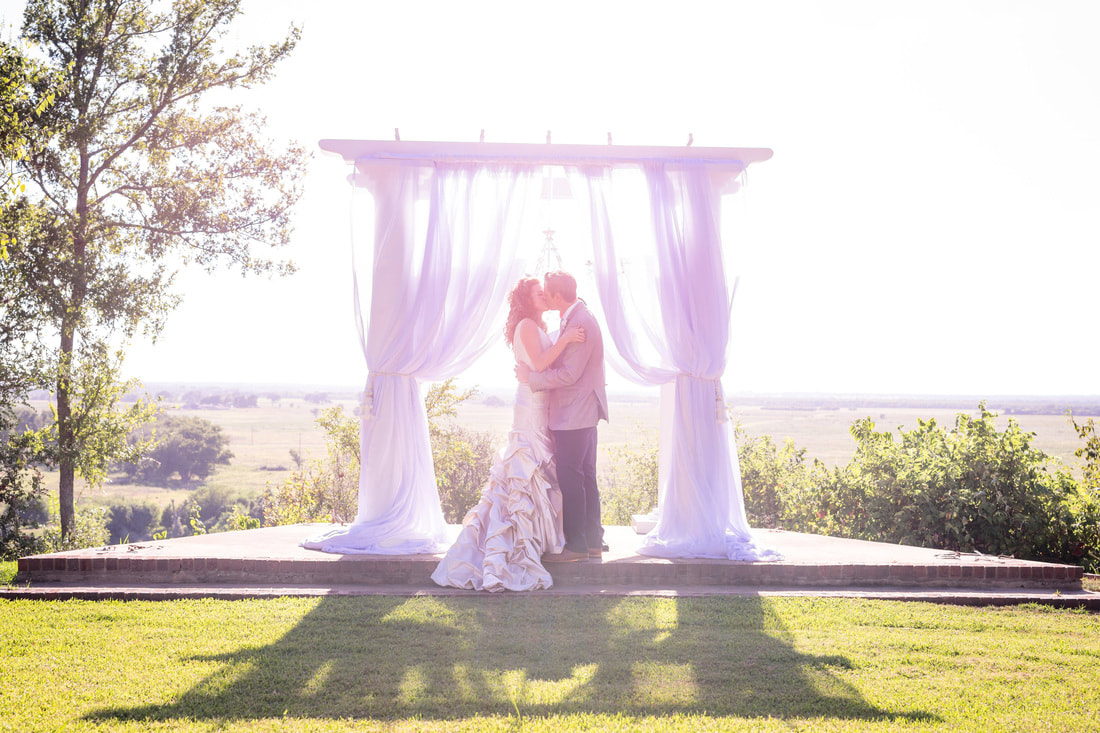Couple kissing at their wedding with archway and curtains at outdoor wedding venue ceremony in hill country.